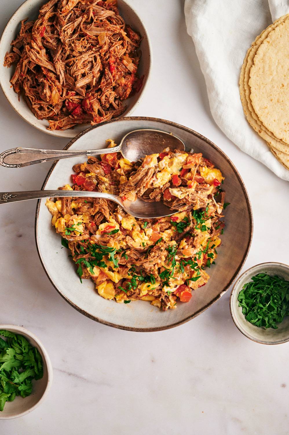 Machaca with eggs with scrambled eggs, tomatoes, peppers, onions, and cilantro in a bowl with tortillas on the side.