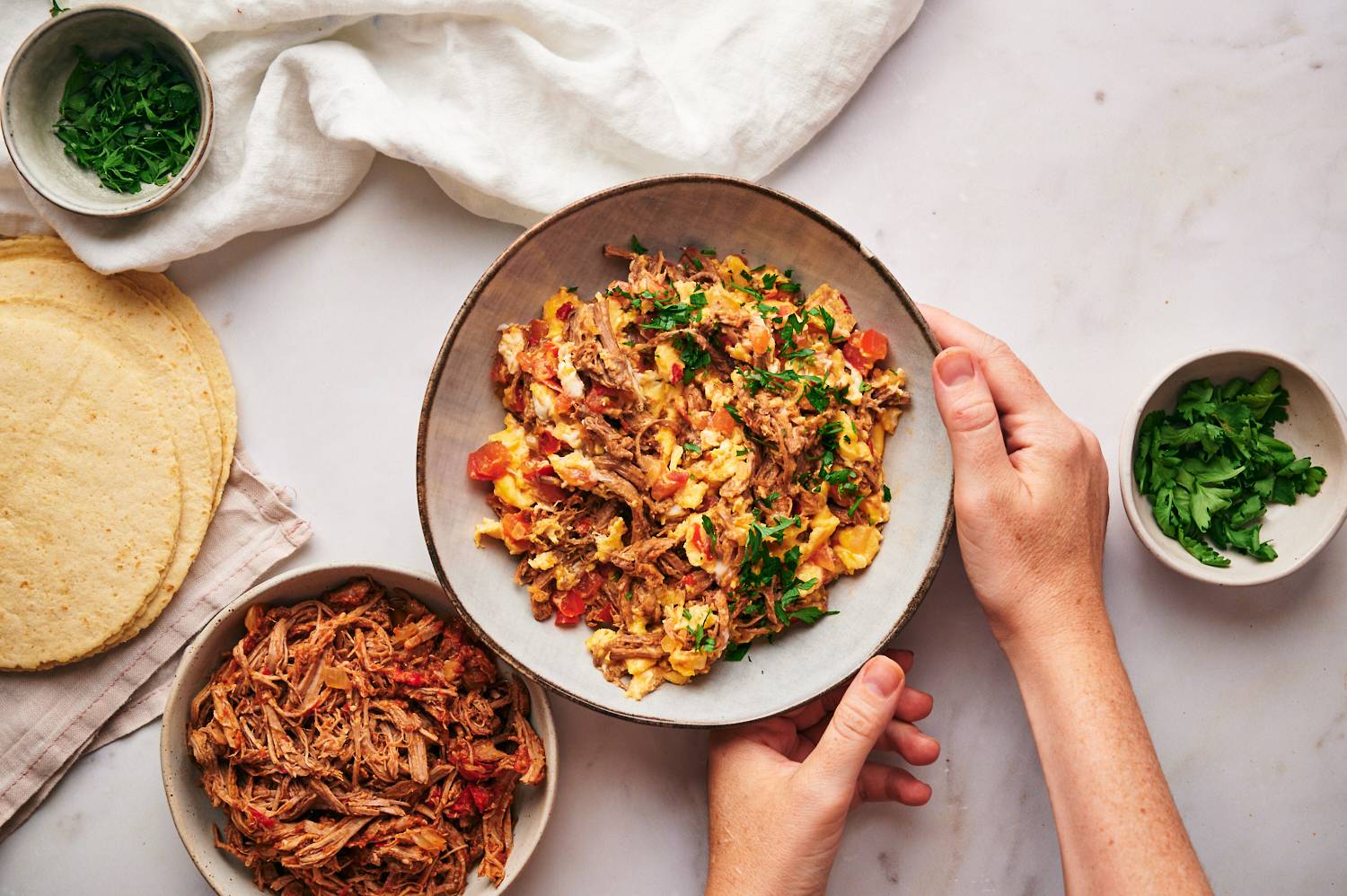 Mexican machaca con huevo served in a bowl with cilantro and tortillas on the side.