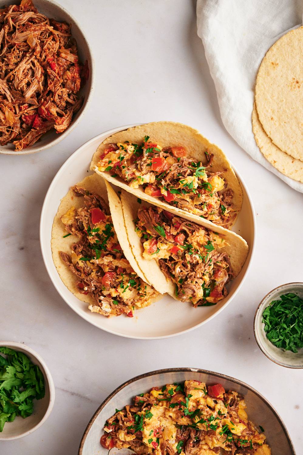 Beef Machaca served with scrambled eggs in three corn tortillas with cilantro, onion, and tomatoes.