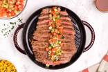 Marinated flank steak served with a tomato, celery, and onion salsa on a grill pan.