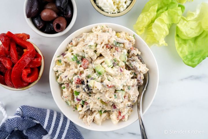 Mediterranean chicken salad with cucumbers, roasted red peppers, dill, parsley, and red onion in a bowl with lettuce on the side.