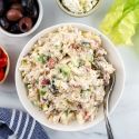 Mediterranean chicken salad with cucumbers, roasted red peppers, dill, parsley, and red onion in a bowl with lettuce on the side.