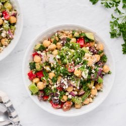 Mediterranean salad with chickpeas, olives, bell peppers, fresh herbs, and feta cheese in a bowl.