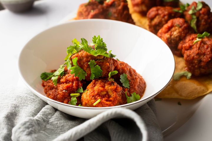 Mexican chipotle meatballs in a spicy tomato sauce in a bowl with chopped cilantro and corn tortillas.