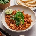 Mexican shredded chicken with tomatoes, spices, and chipotle peppers in a bowl with avocado, lime, and corn tortillas.