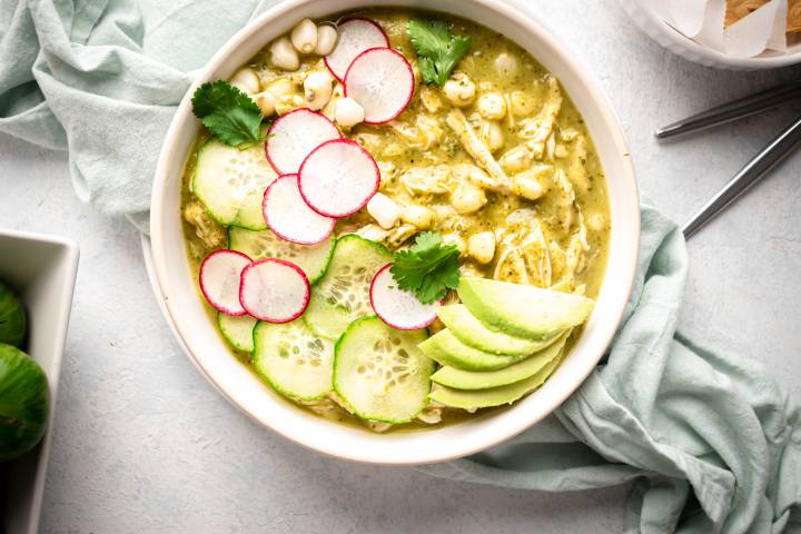 Green chicken pozole in a bowl with avocado, radish, cilantro, chicken, and hominy.