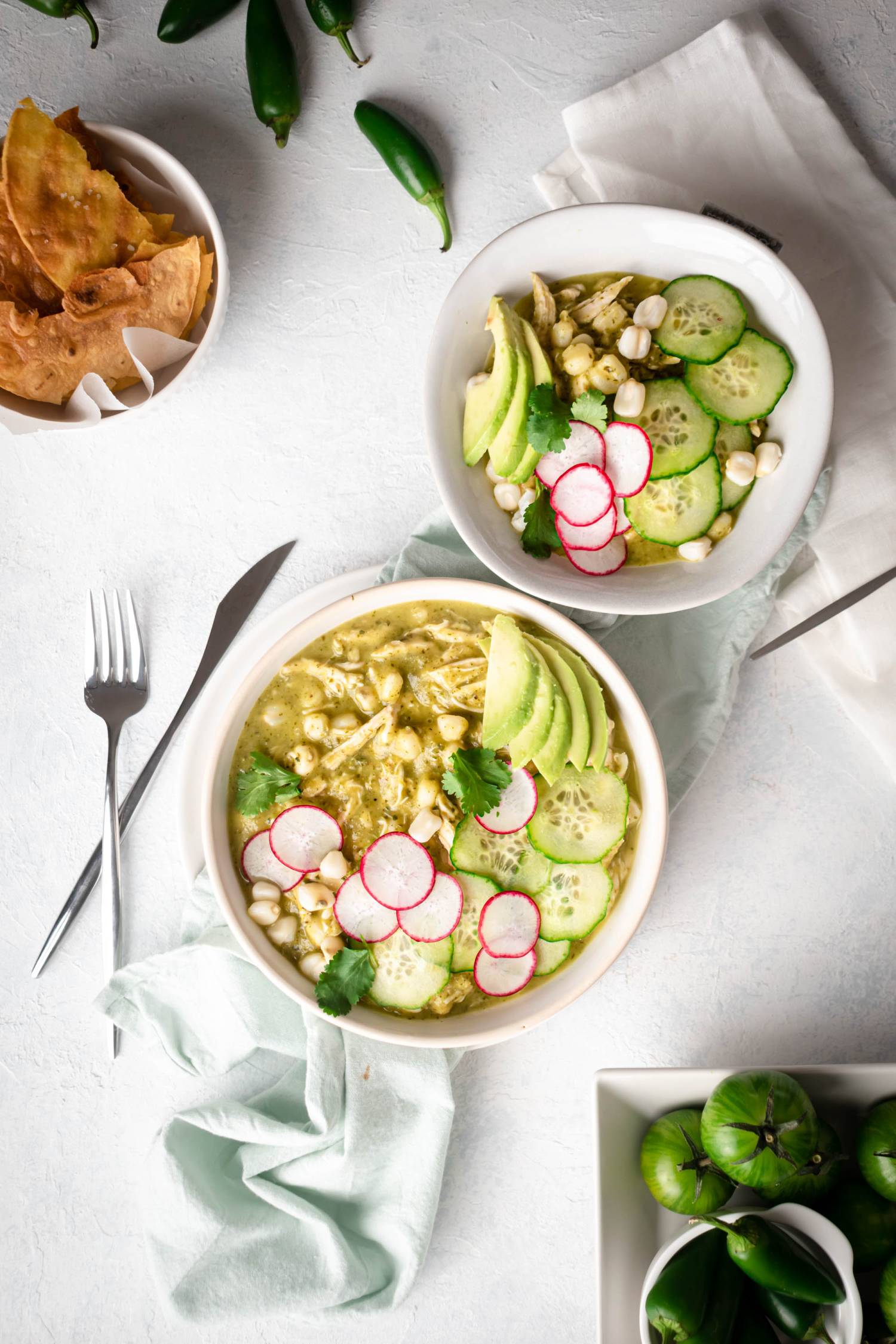 Pozole verde in two bowls with hominy, shredded chicken, avocado, lime, and and cilantro.