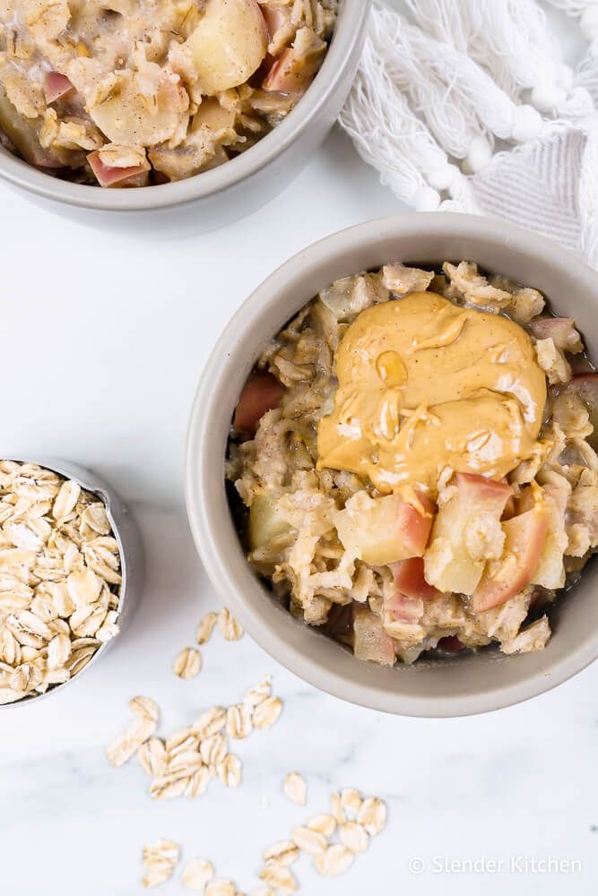 Microwave oatmeal with apples, cinnamon, and peanut butter in a bowl with oats on the side.