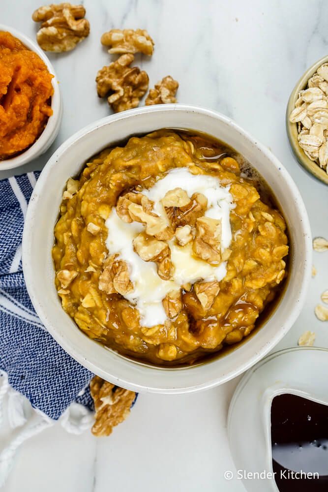 Pumpkin pie oatmeal with pumpkin puree, oats, walnuts, and maple syrup in a bowl with a blue napkin.