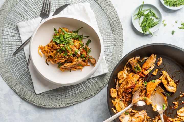 Moo shu pork with thinly sliced pork, cabbage, and mushrooms in a soy based stir fry sauce in a bowl and a skillet.