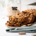 Oatmeal banana bread with chocolate chips sliced on a plate with a blue cloth napkin.