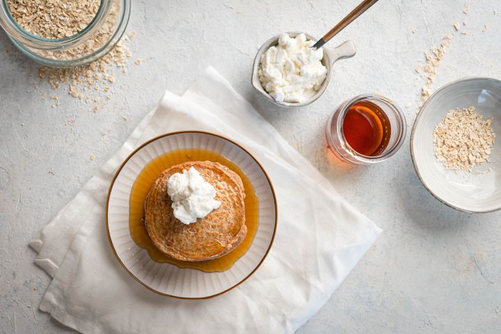 Oatmeal protein pancakes made with rolled oats, egg whites, and cottage cheese stacked on a plate with maple syrup and whipped cream.