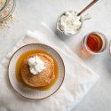 Oatmeal protein pancakes made with rolled oats, egg whites, and cottage cheese stacked on a plate with maple syrup and whipped cream.