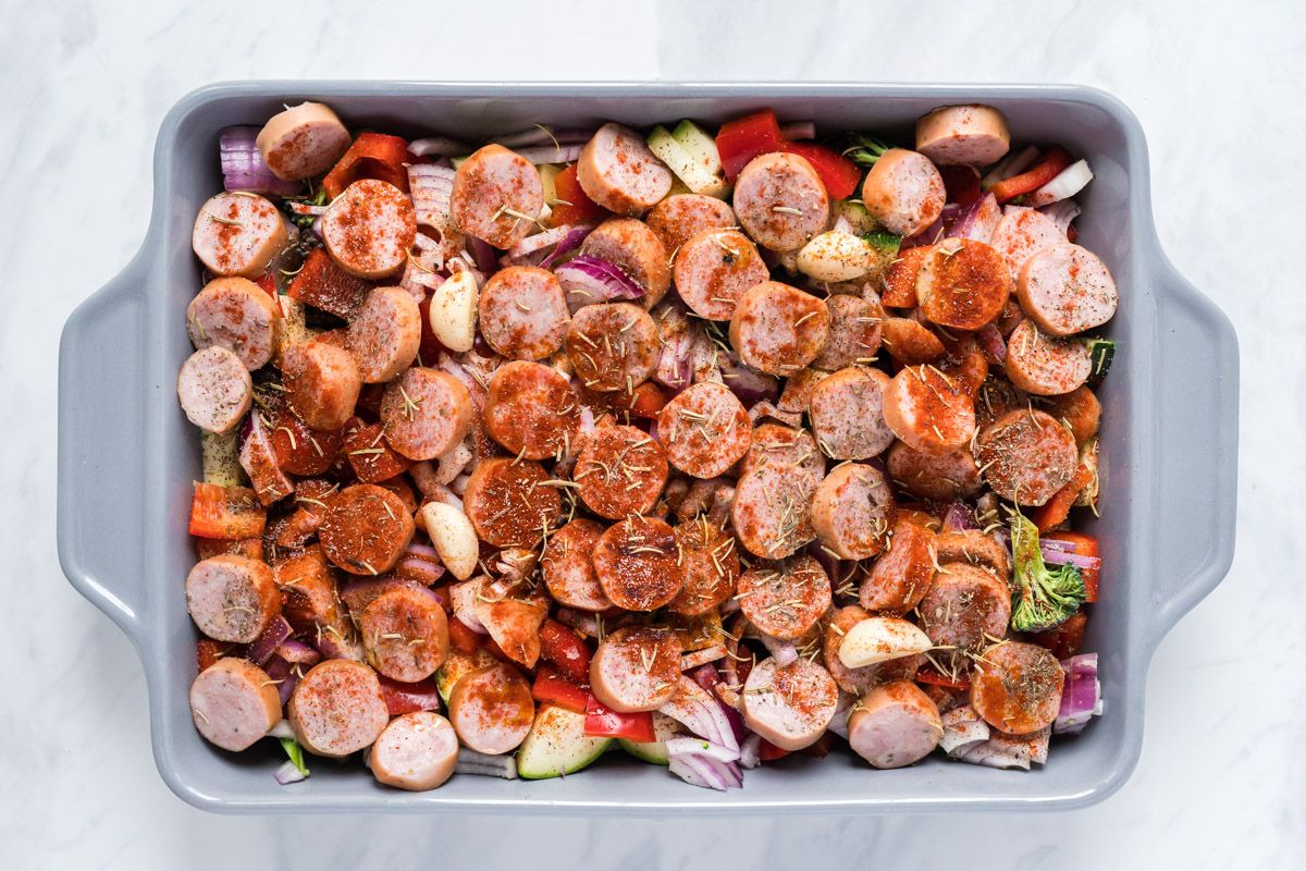 Sausage with onions, potatoes, peppers, and zucchini in a baking dish with seasoning and rosemary. 