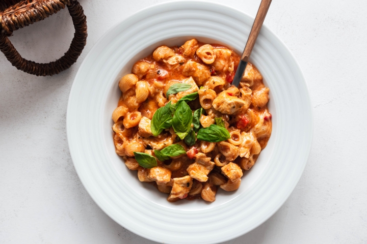 One pot chicken pasta with marinara sauce, chicken breast, melted cheese, and fresh basil in a bowl.