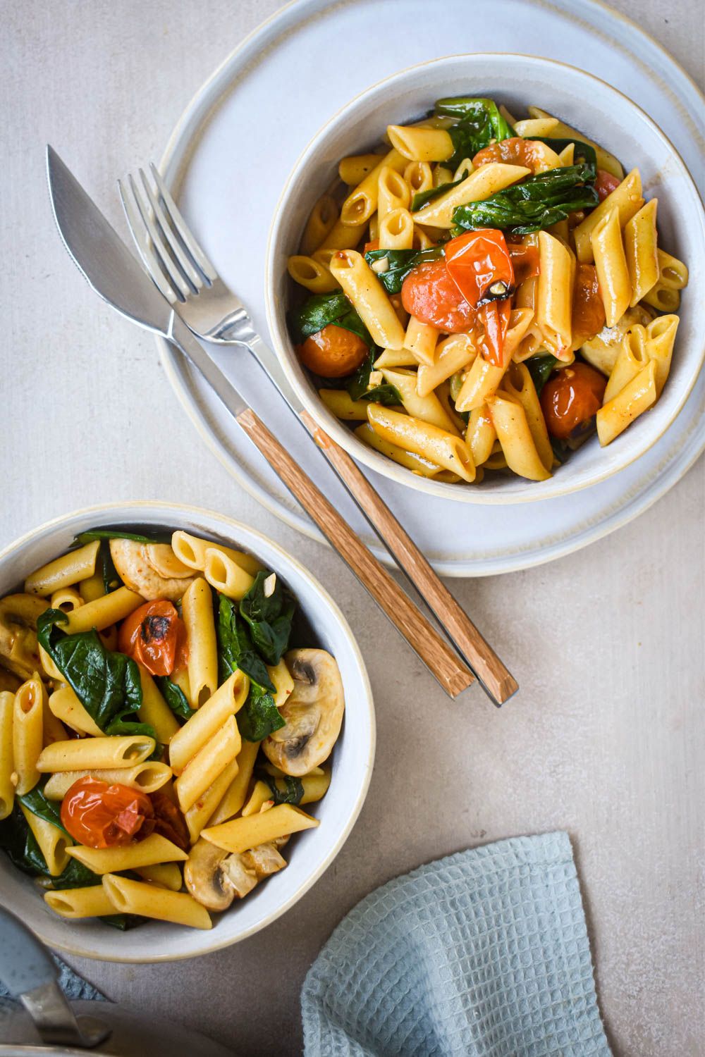 Tomato and basil pasta cooked in one pot with spinach, mushrooms, and garlic served on two plates.