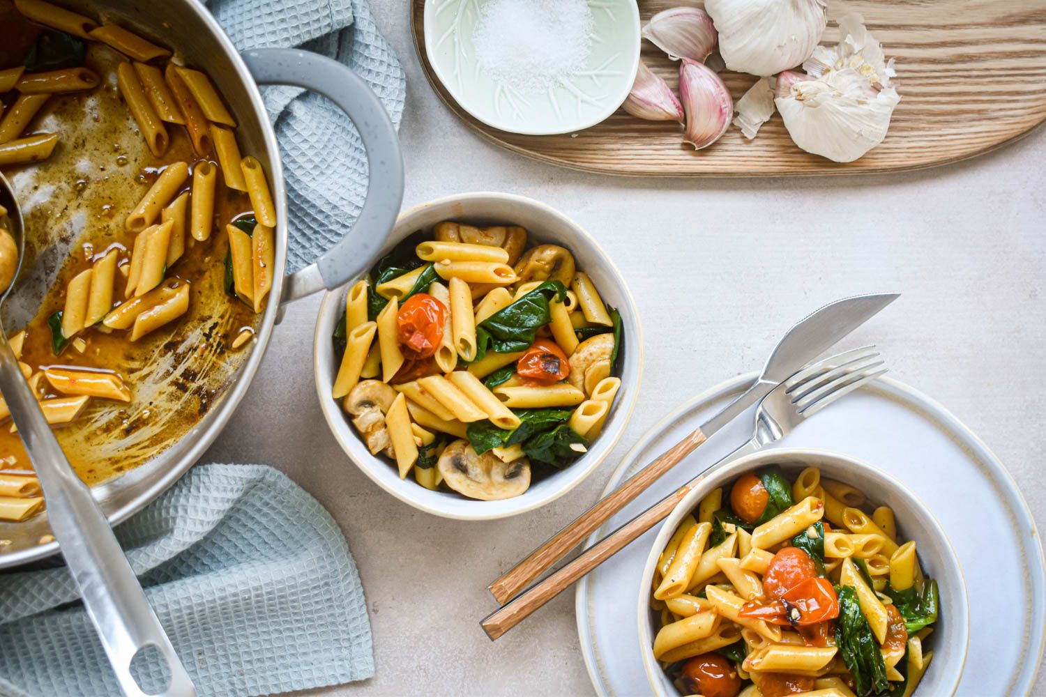 Pasta with tomatoes and basil in two bowls with fresh spinach and mushrooms.