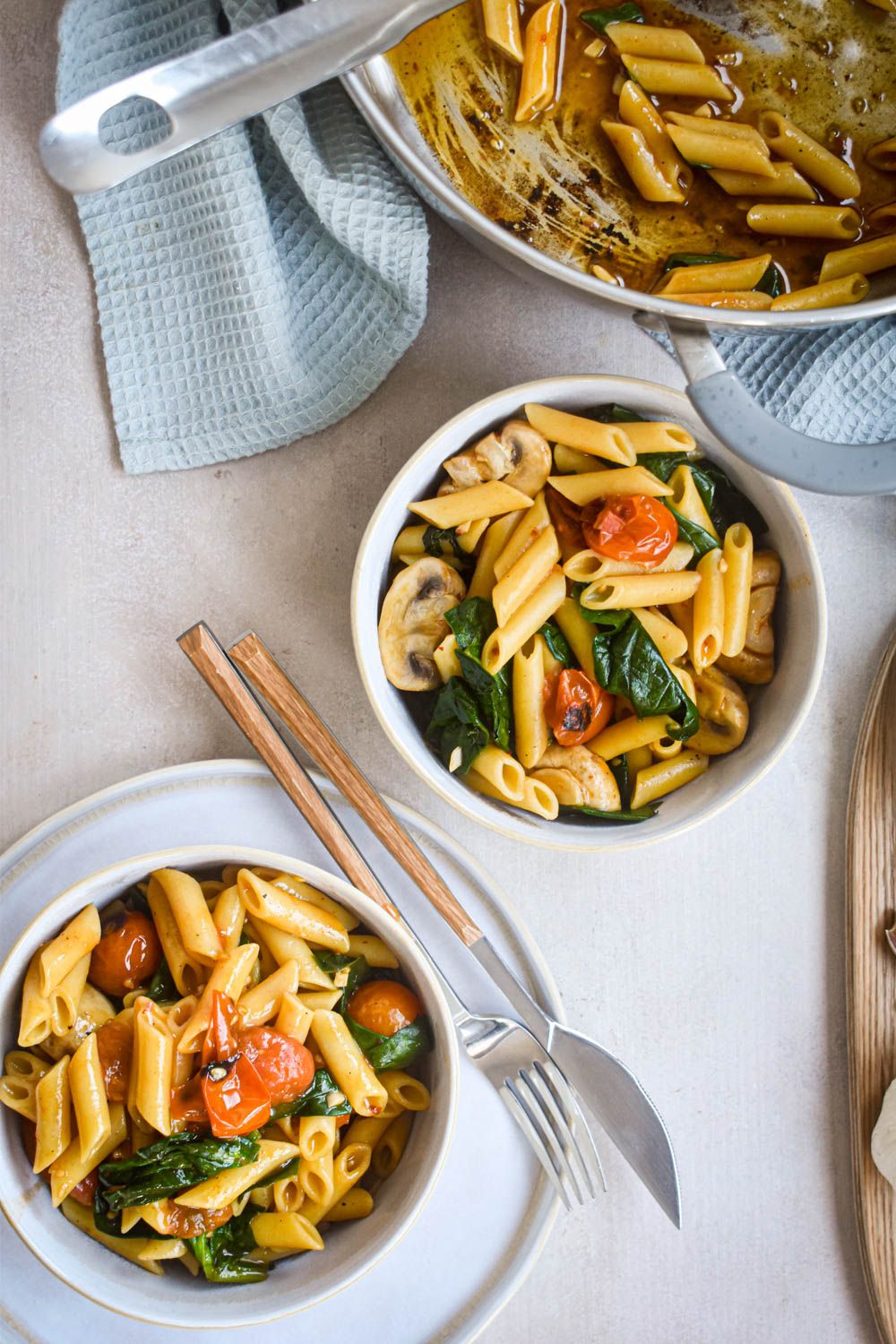 Tomato basil pasta with cherry tomatoes, spinach, and mushrooms in two bowls with a fork and knife.