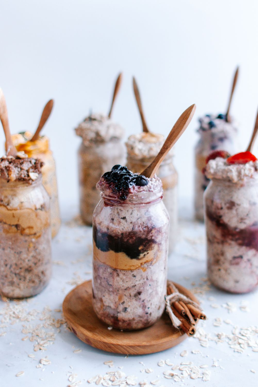 Various flavors of overnight oats in mason jars with fresh fruit and small wooden spoons.