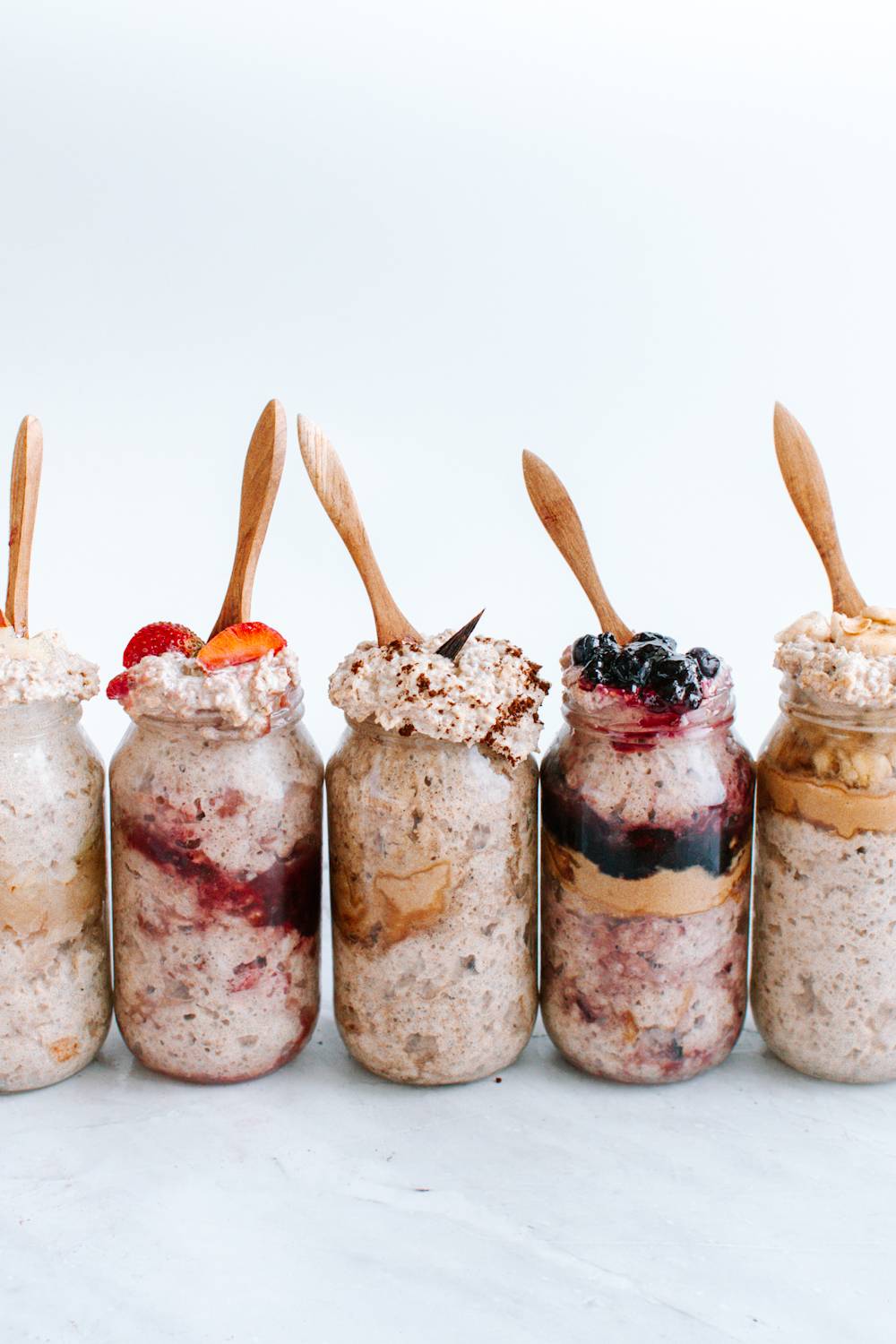 Mason jars with overnight oatmeal including bananas, blueberry, strawberry, and more.