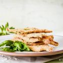 Parmesan crusted chicken piled on a plate with fresh basil and a fork.