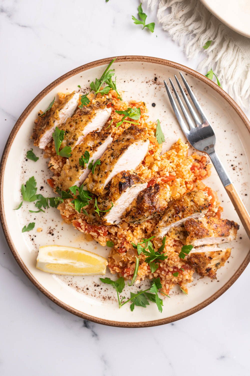 Keto Parmesan chicken with cauliflower rice served on a plate with tomatoes, lemon, and parsley.