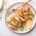 Garlic parmesan chicken breast and cauliflower rice on a plate with fresh parsley and lemon.