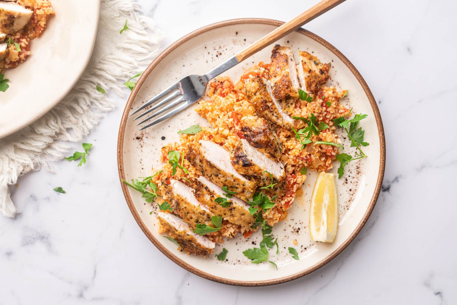 Garlic parmesan chicken breast and cauliflower rice on a plate with fresh parsley and lemon.