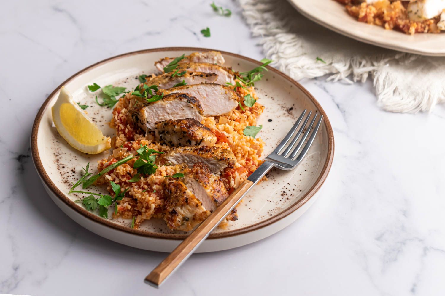 Low carb garlic Parmesan cauliflower rice with sliced chicken breast served with parsley and lemon.