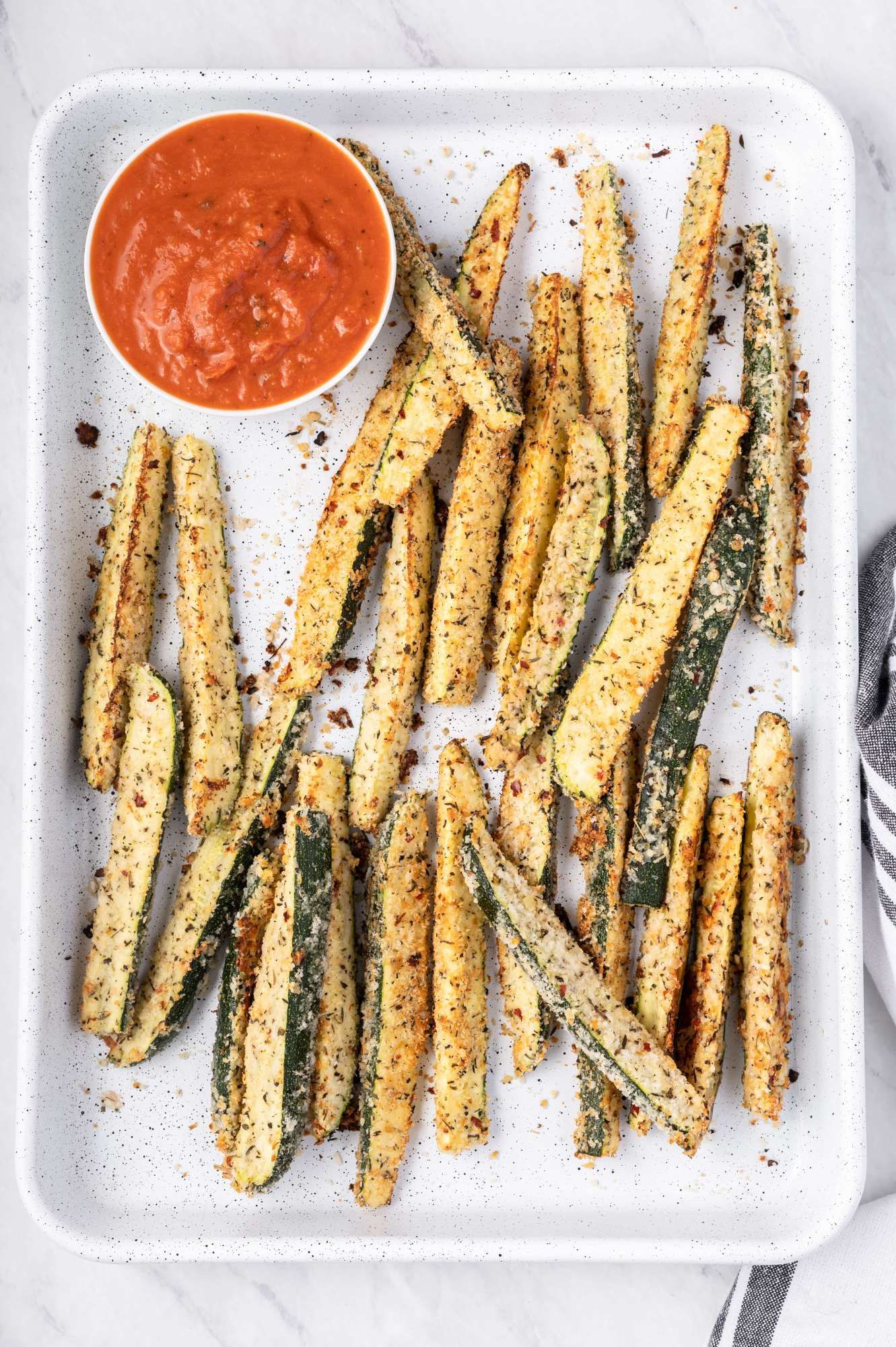 Oven baked parmesan zucchini fries on a baking sheet with marinara sauce.