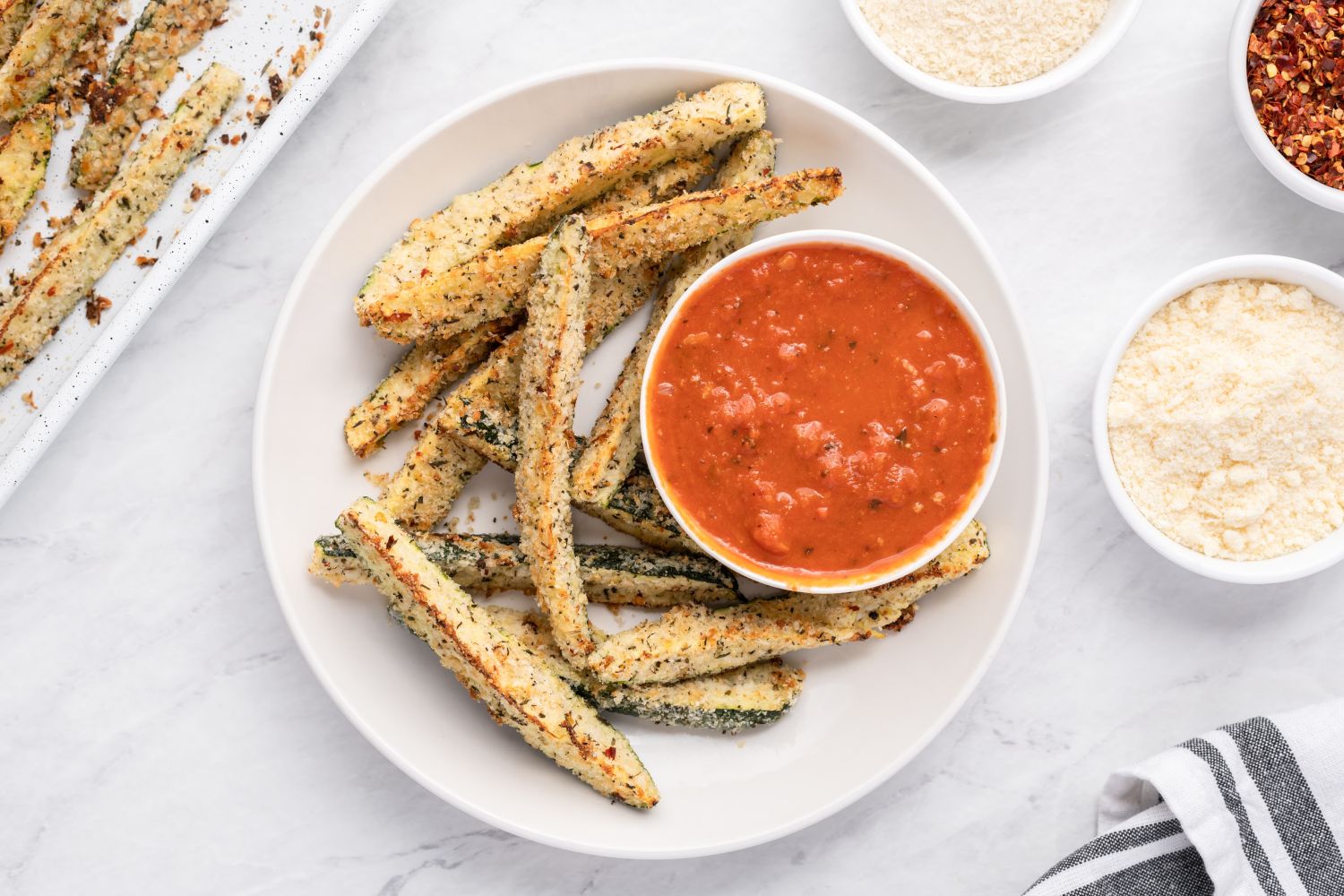 Baked Parmesan zucchini fries with a crispy panko breading on a white plate with marinara sauce.