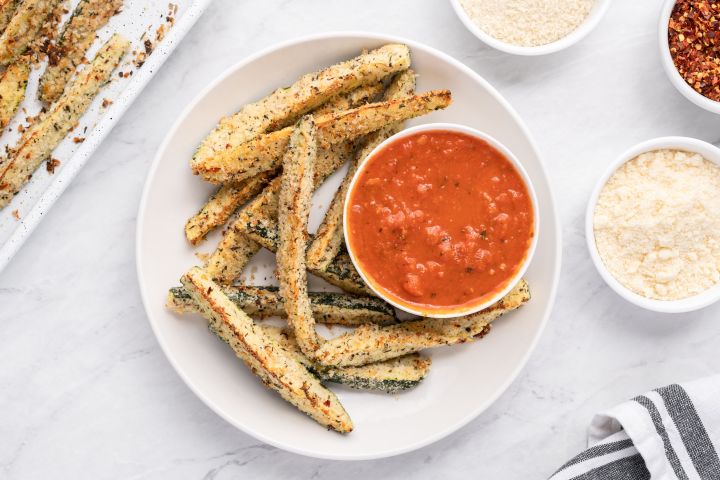 Baked Parmesan zucchini fries with a crispy panko breading on a white plate with marinara sauce.