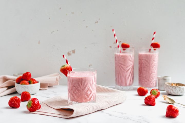 PB&J Smoothie with Greek yogurt in three glasses with fresh strawberries and peanut butter on the side.