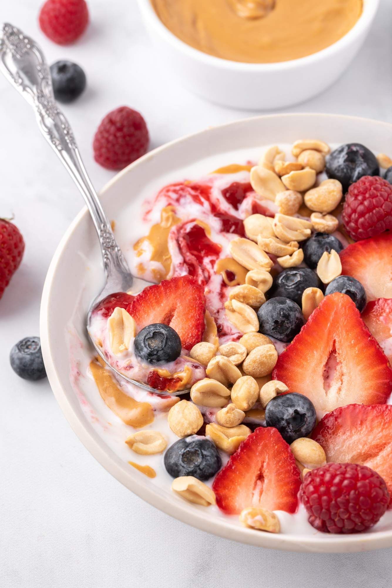 PB&J greek yogurt bowl with fresh berries, peanut butter, chopped nuts, and jelly in a white bowl.