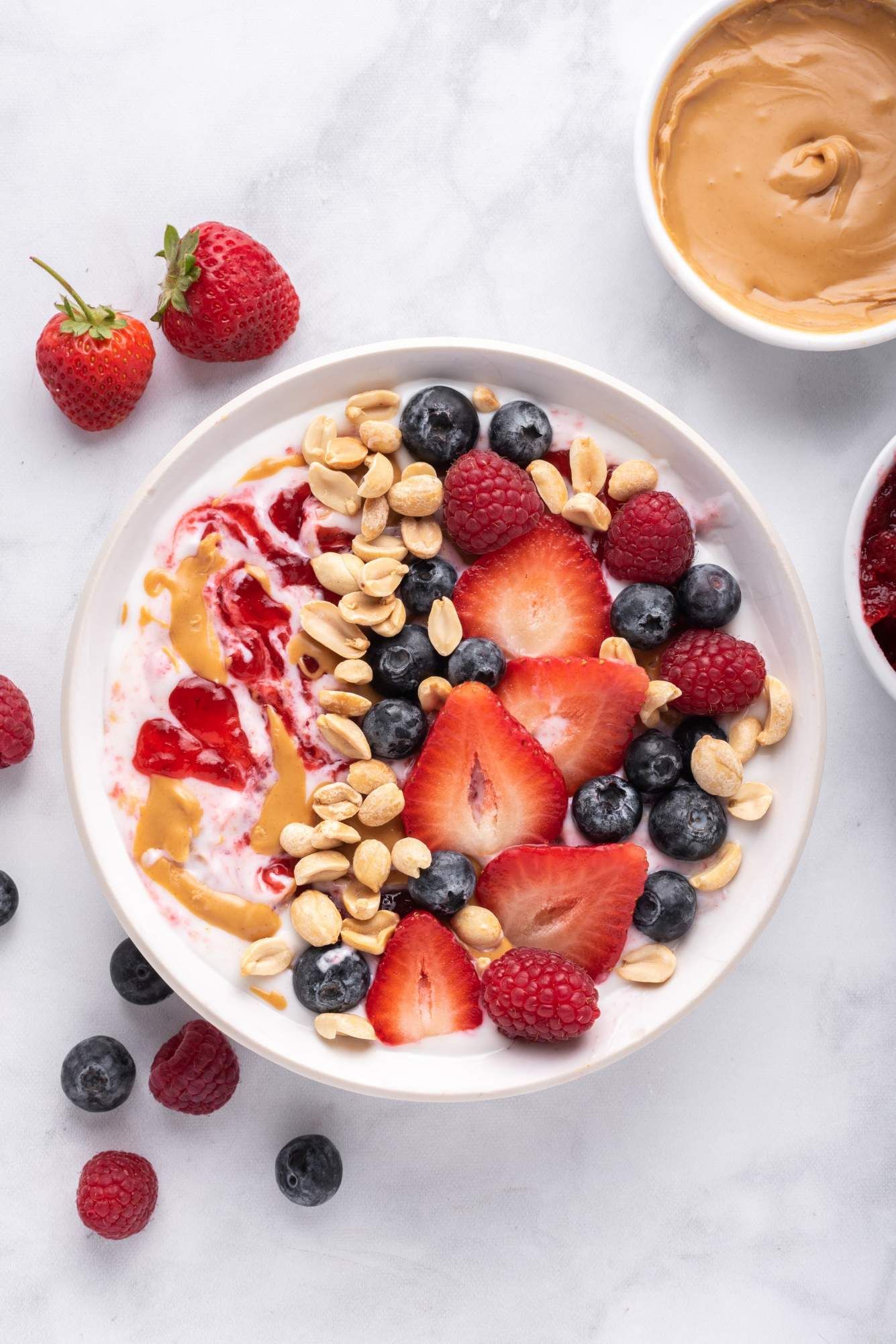 Greek yogurt bowls with peanut butter, jelly, and fresh fruit in a white bowl.