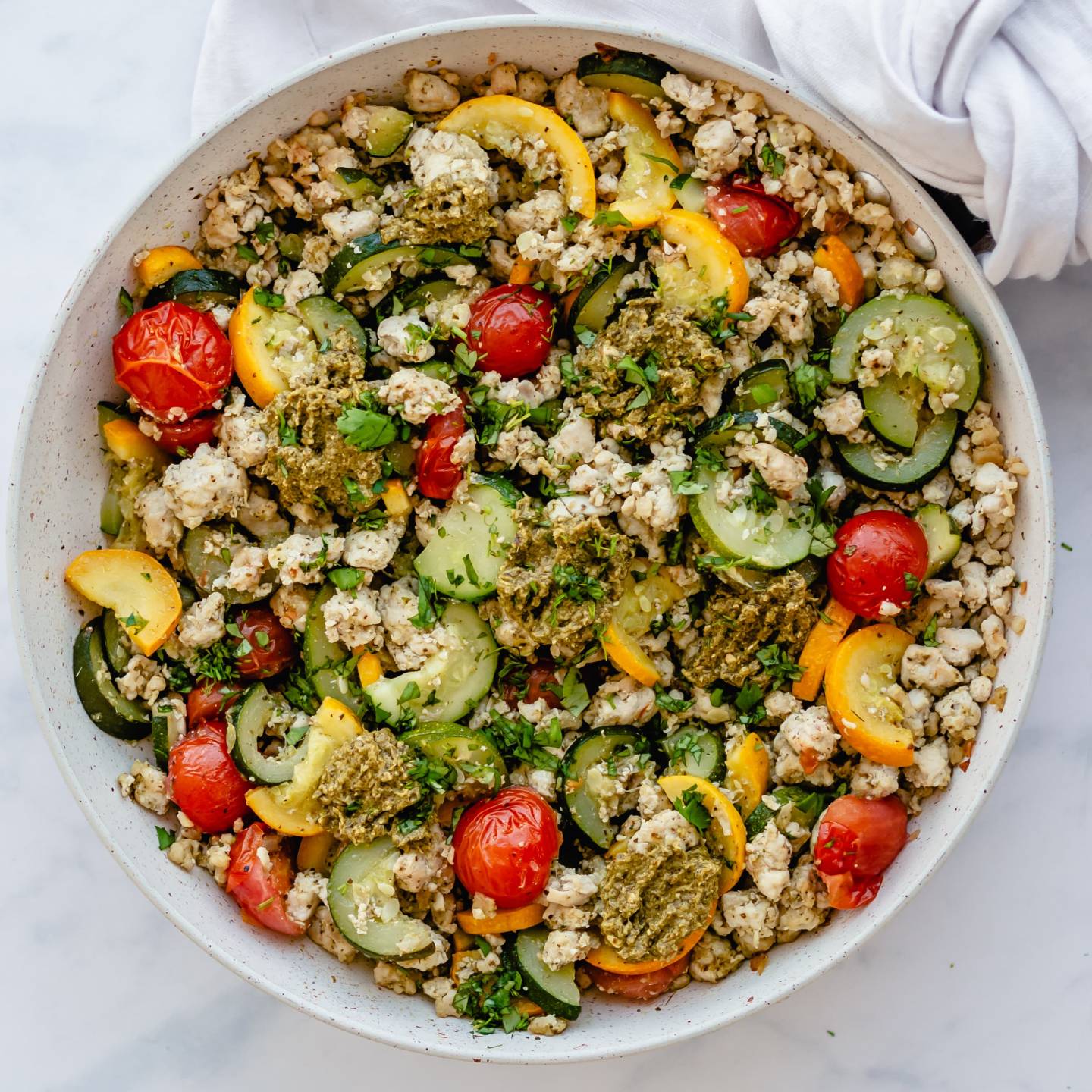 Ground turkey, zucchini, yellow squash, and cherry tomatoes in a skillet and topped with pesto.