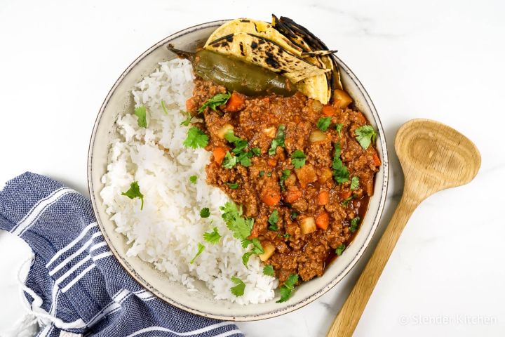 Picadillo with potatoes, carrots, and chipotle tomato sauce in a bowl with rice, tortillas, and cilantro.