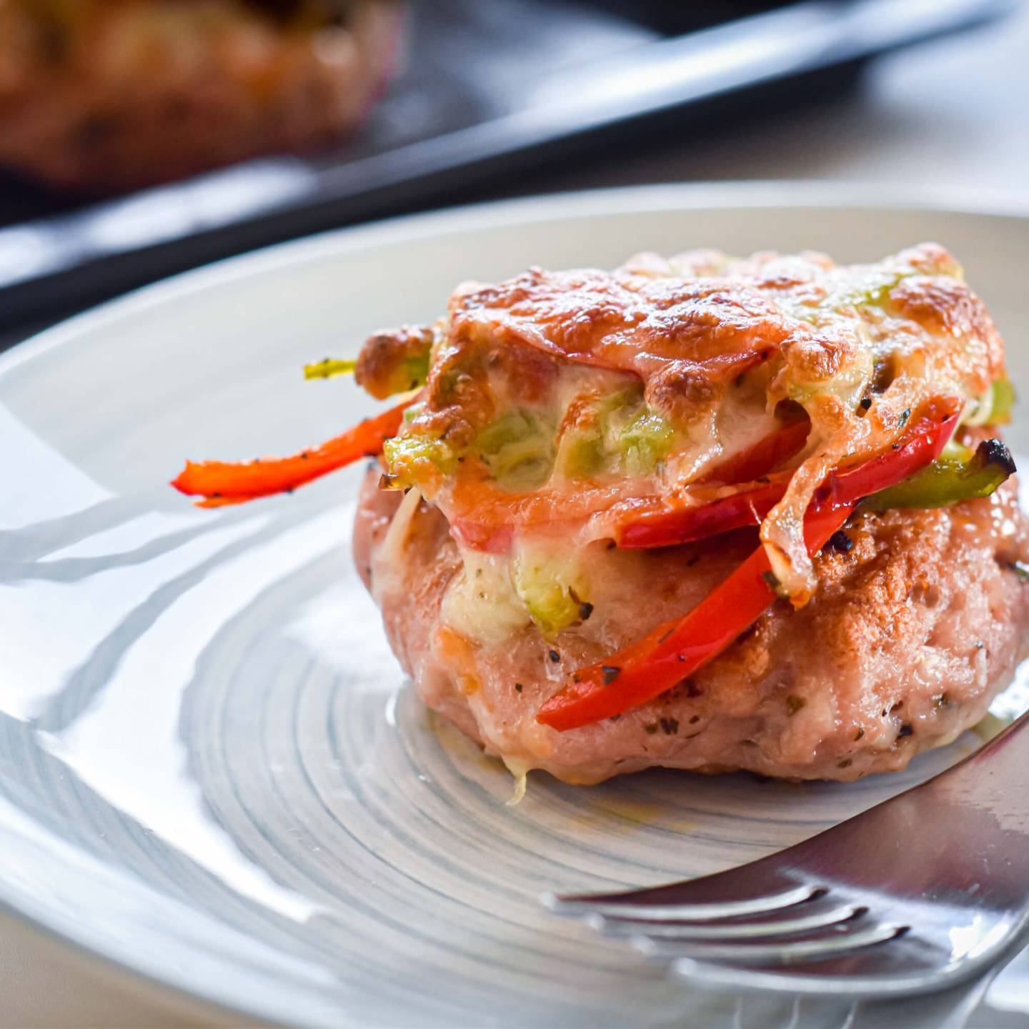 Pizza turkey burgers with marinara sauce, melted cheese, peppers, onions, and basil on a plate with a fork.