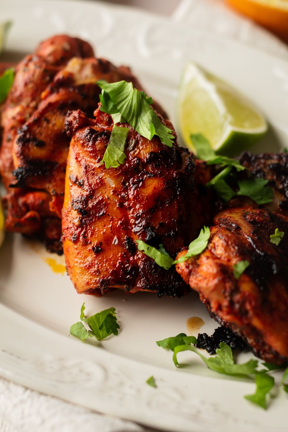 Mexican grilled chicken served on a white plate with fresh limes and cilantro.