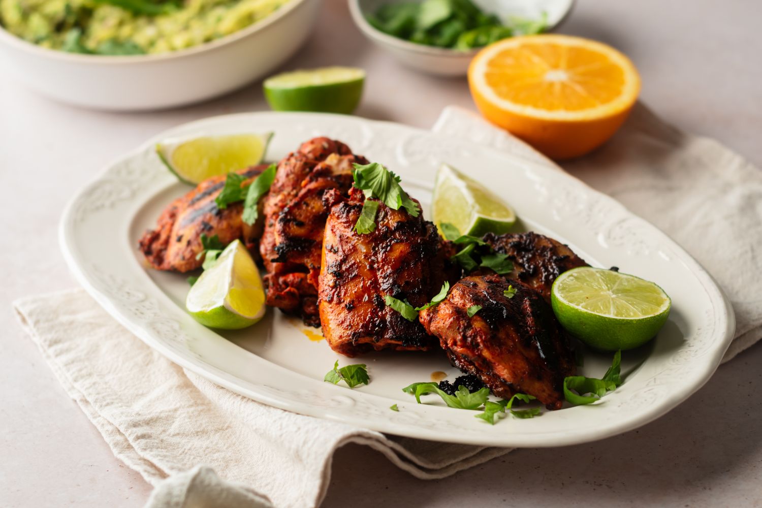 Pollo asado made with chicken thighs marinated in achiote paste and citrus juice served on a plate with guacamole and pickled onions.