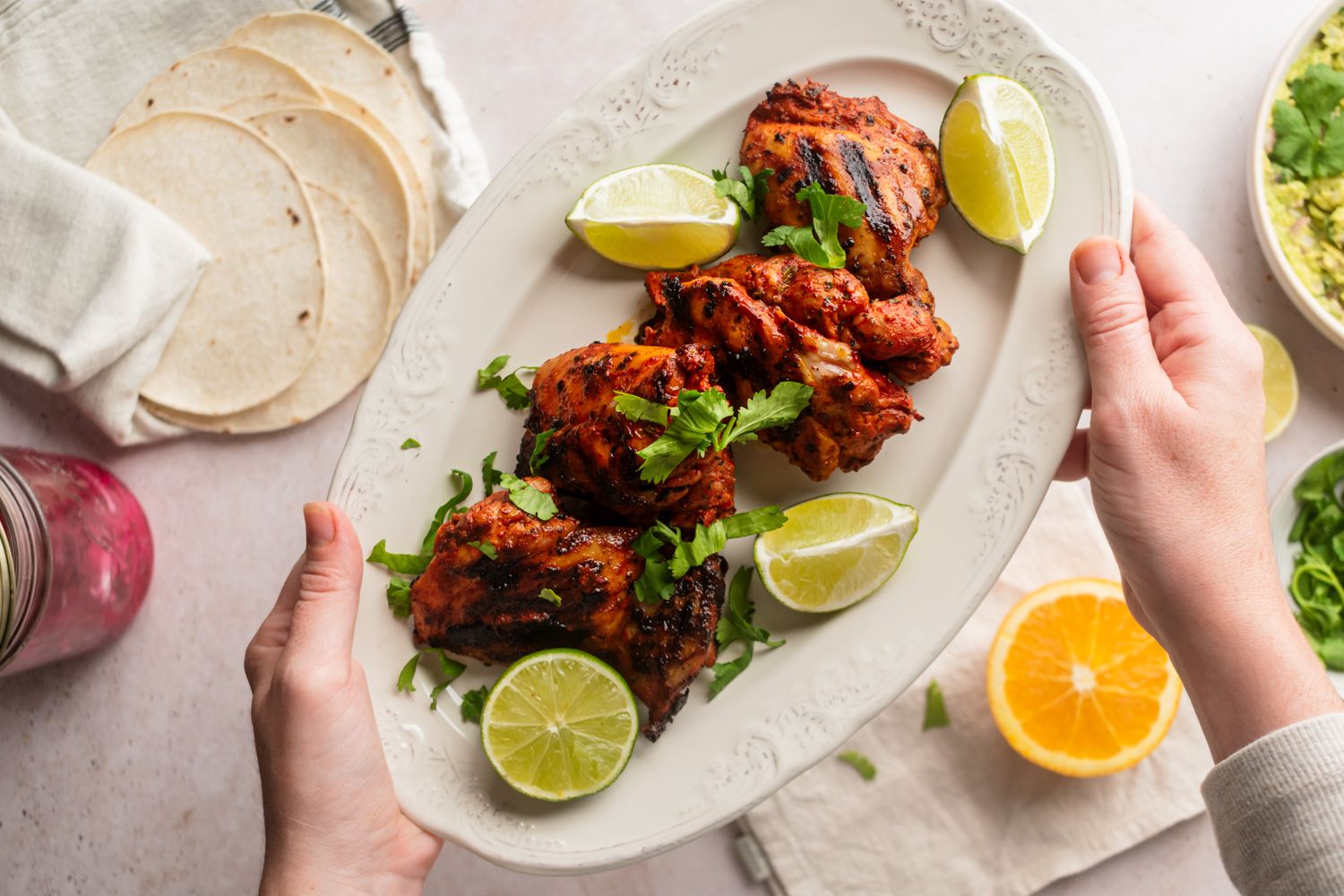 Grilled Pollo Asado with a dark red achiote marinade on a plate with limes, cilantro, tortillas, and guacamole.