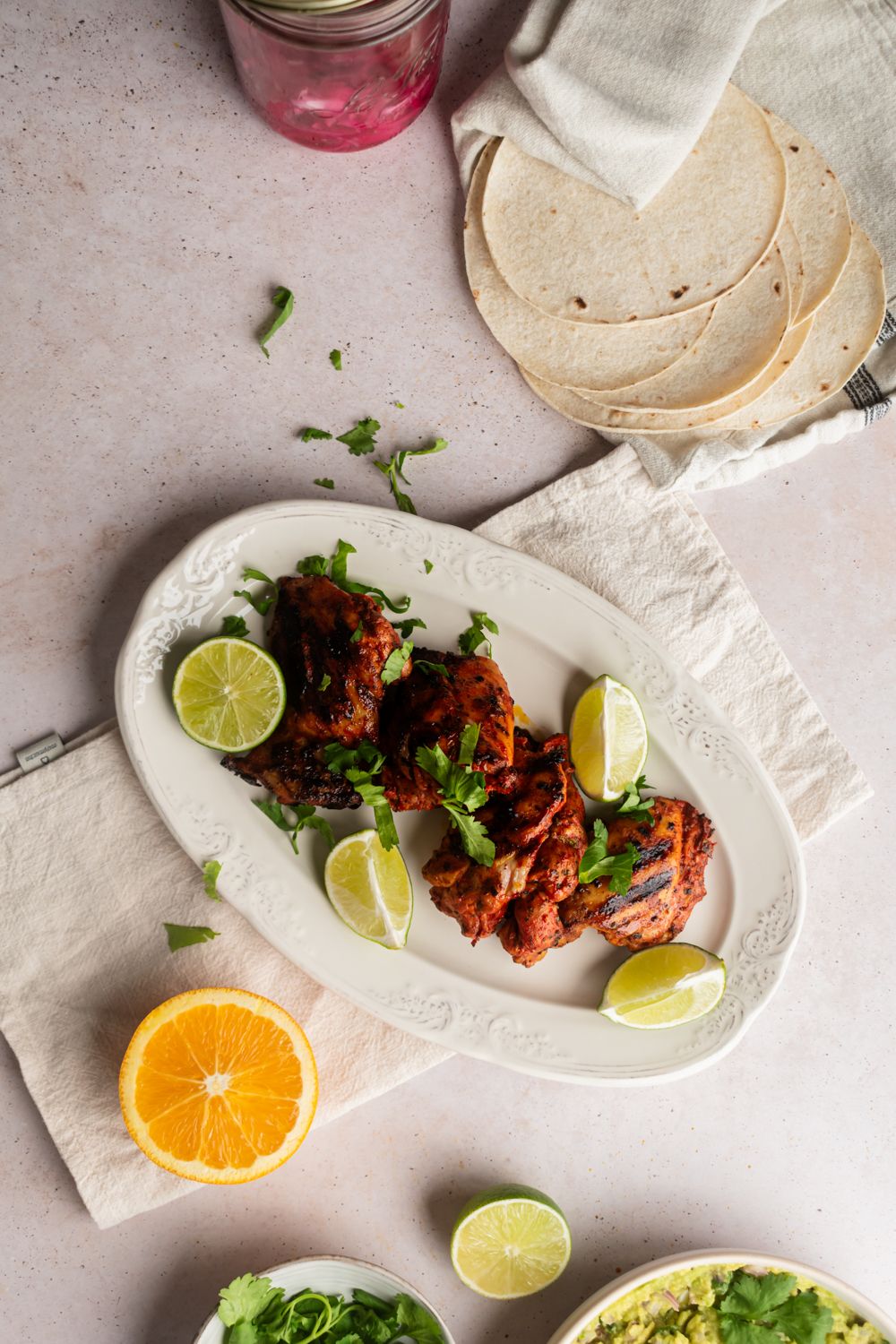 Mexicano Pollo Asado with grill marks on a plate with limes, oranges, tortillas, pickled onions, and corn tortillas.