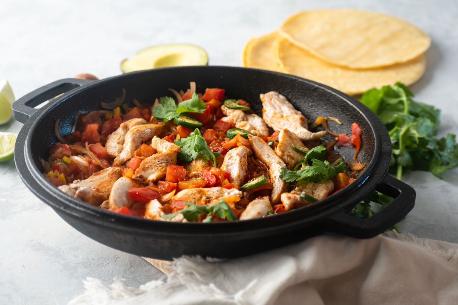 Skillet with chicken in ranchero sauce served with cilantro, lime, and corn tortillas.