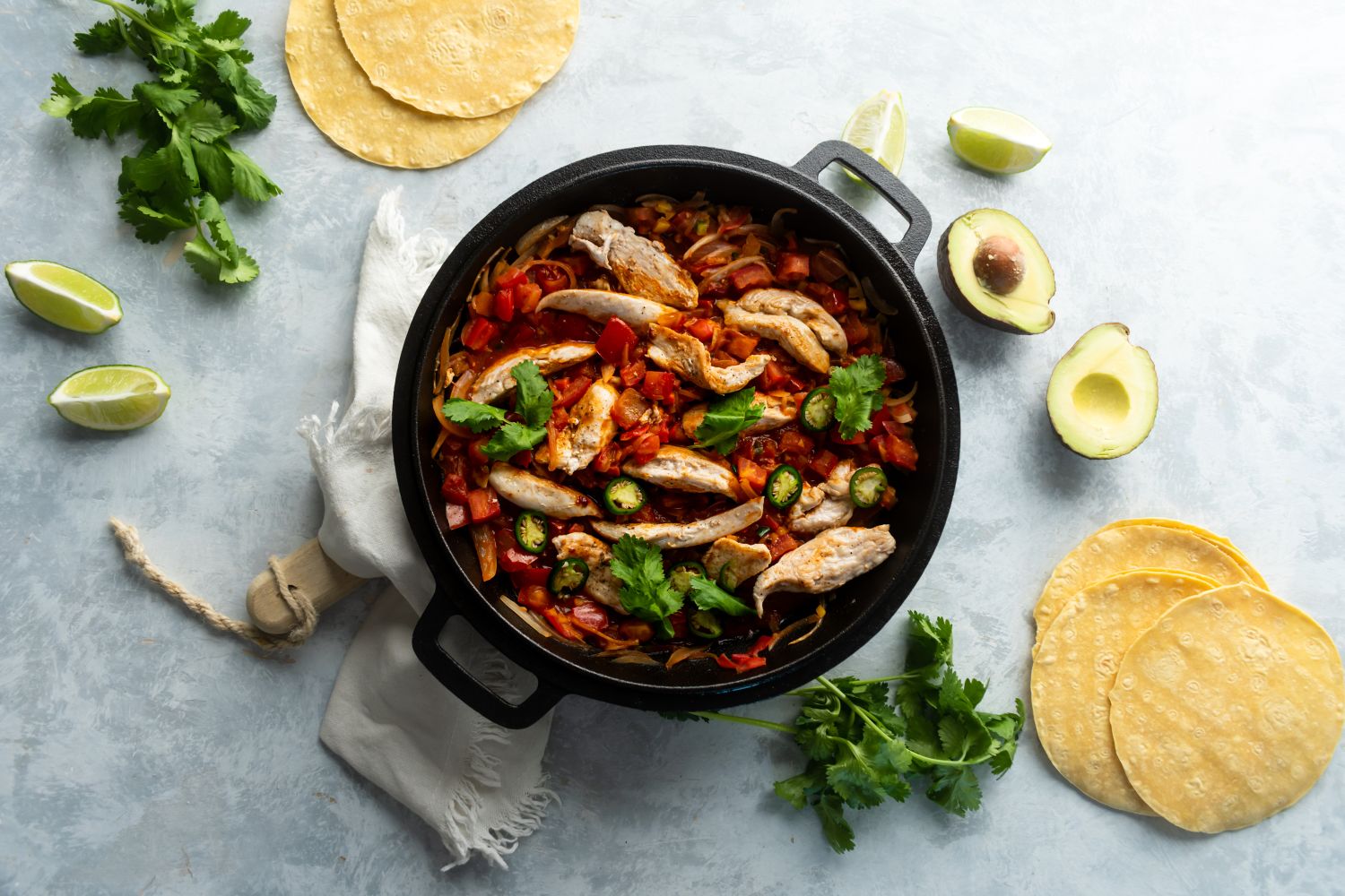 Pollo ranchero with chicken breast, tomato ranchero sauce, jalapeños, and cilantro in cast iron skillet.