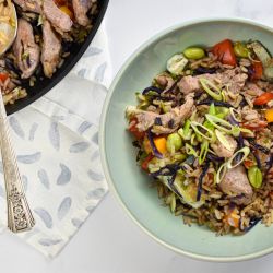 Pork fried rice with pork tenderloin, brown rice, carrots, peas, cabbage, and eggs in a bowl.