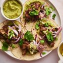 Pork tacos with crispy pork, red onions, cilantro, and avocado on a plate.