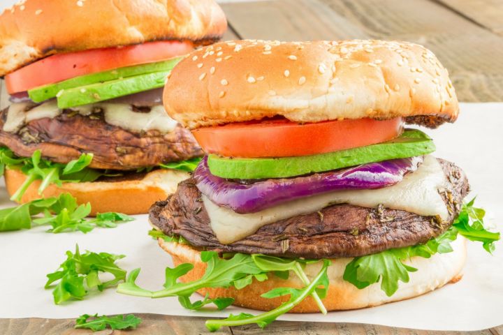 Portobello burgers with avocado, swiss cheese, tomatoes, and lettuce on a bun.