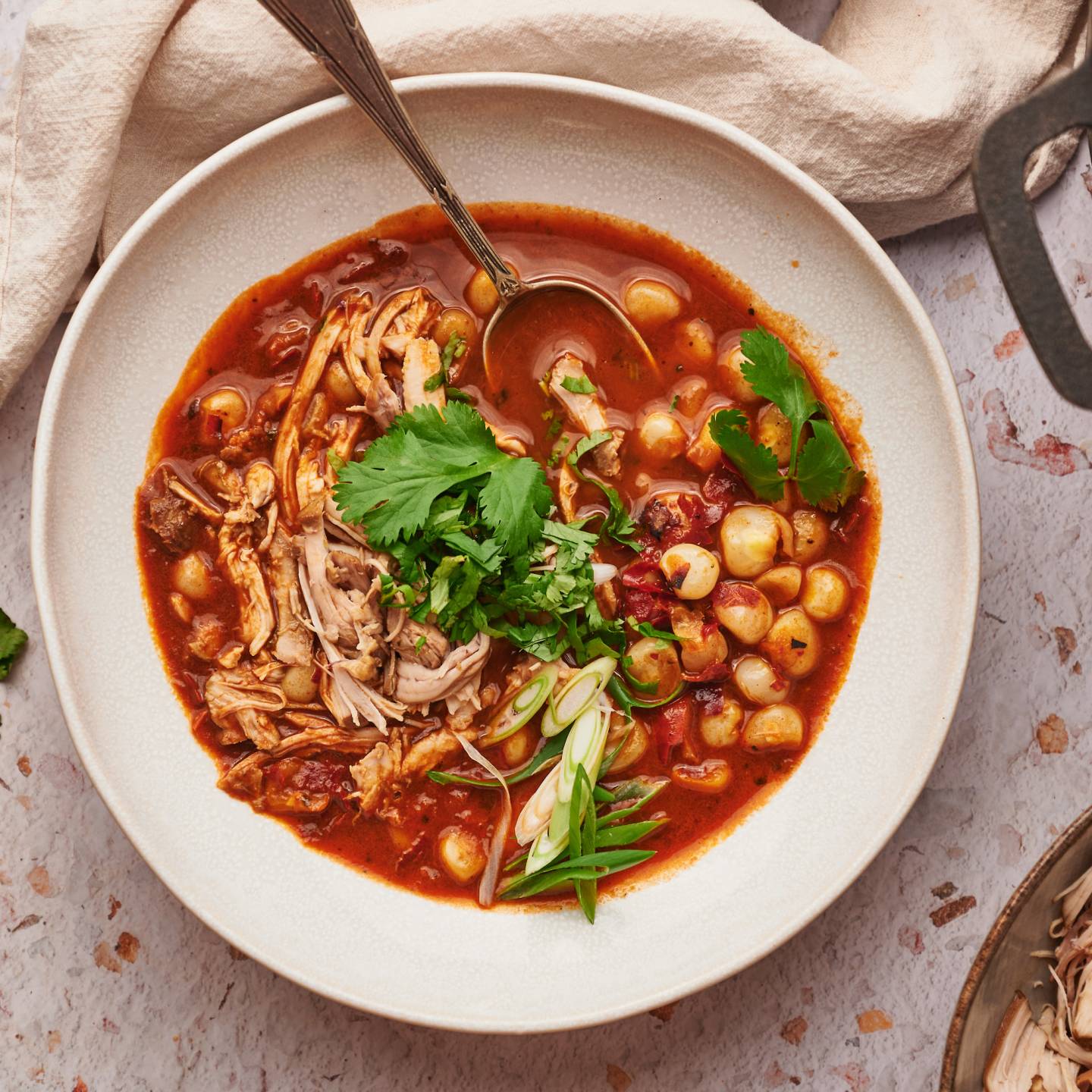 Red chicken pozole in a bowl with shredded chicken, hominy, red chile broth, avocado, and limes. 