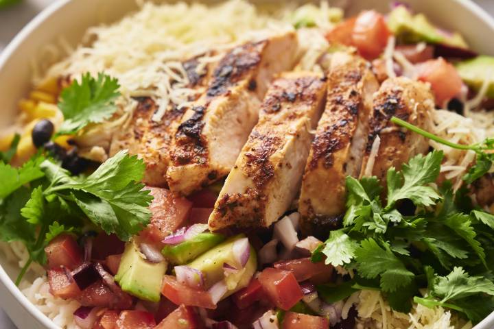 Rice bowl with cooked chicken, black beans, corn, pico de gallo, avocado, and cheese.