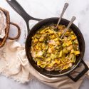 Rajas con queso in a skillet with poblano peppers, red onion, corn, and cheese sauce. with flour tortillas on the side.